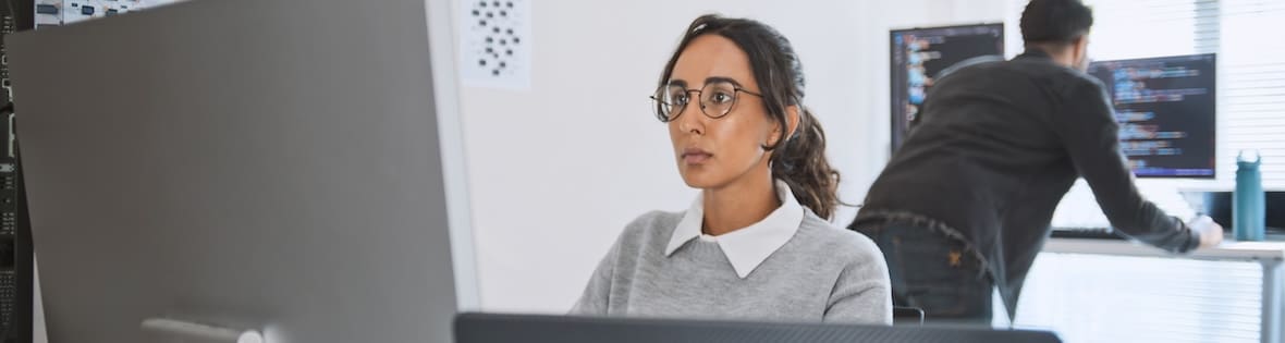 Woman working at a computer screen while a man behind her reviews code.