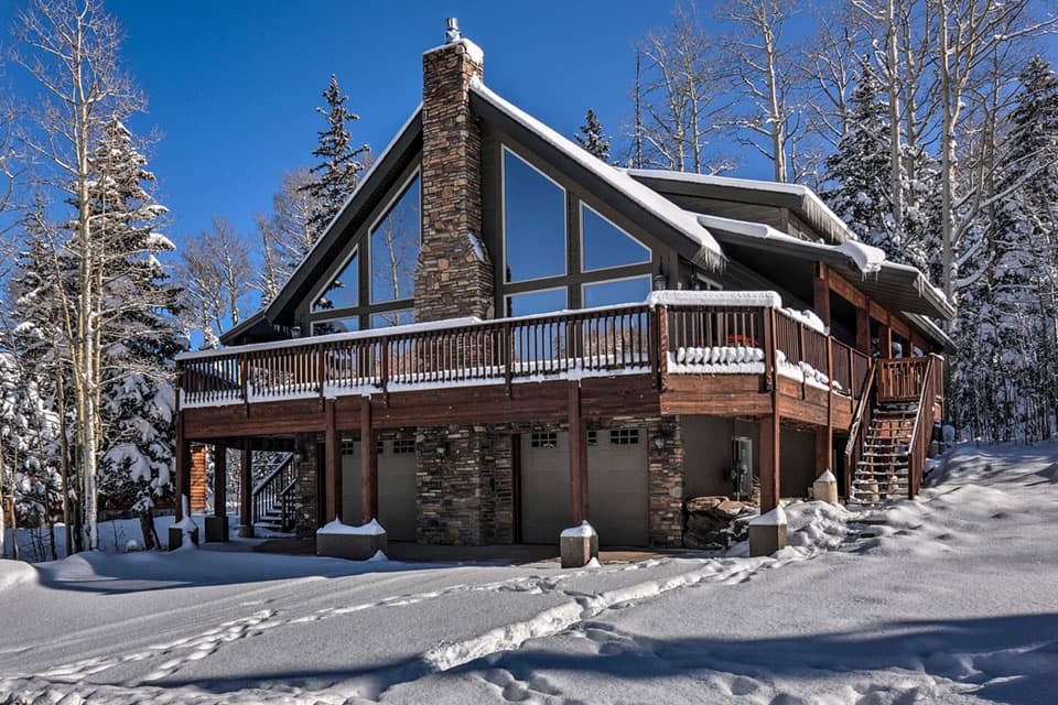 A mountain cabin in the snow set against a backdrop of pines.
